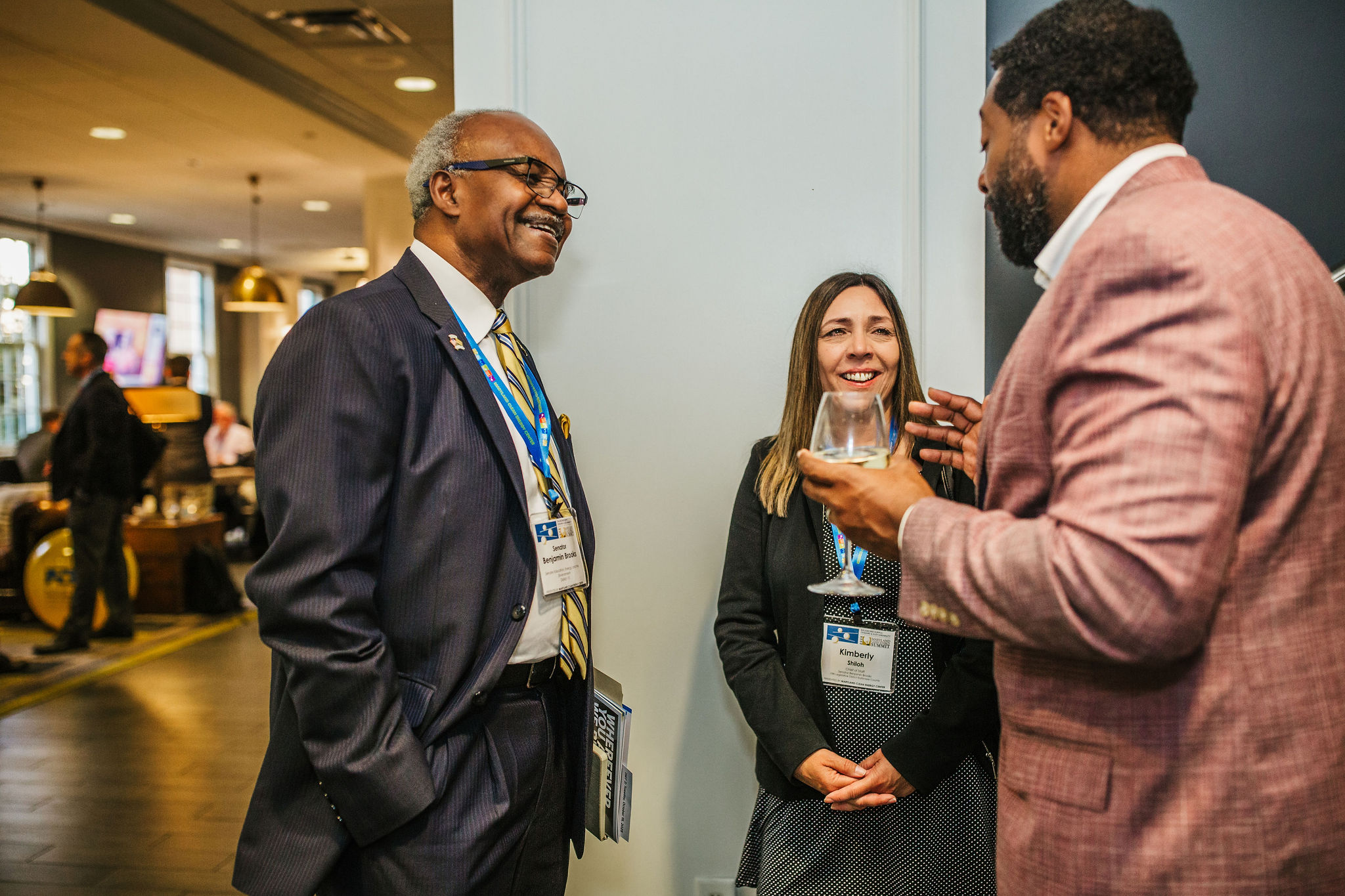 Three people are engaged in conversation at a social event. The setting appears to be a modern indoor space.