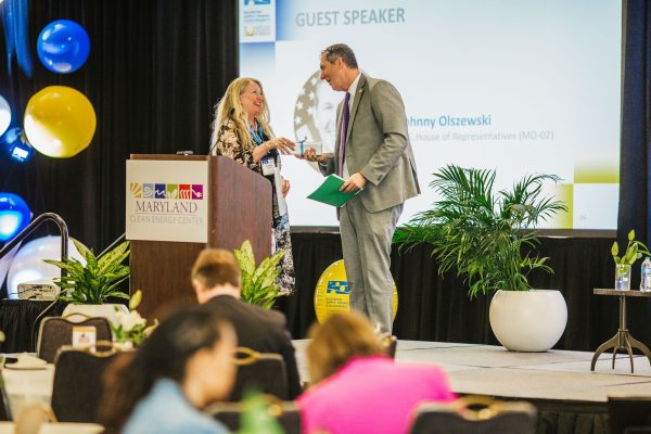 A woman and a man are standing on stage at a conference, engaging in conversation.