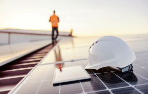 A hardhat and tablet sitting on a solar panel with a construction working walking away.