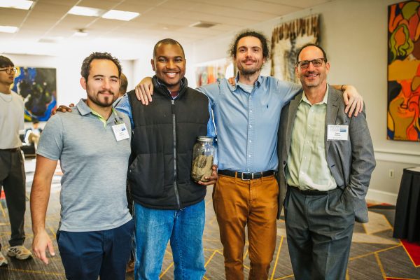 Four men stand together, smiling and posing for the camera at a conference.