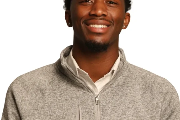 A young man with short, curly hair smiles while wearing a light gray zip-up sweater over a white shirt. The background is plain white