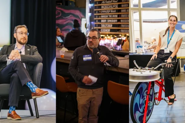 A man in a suit with colorful socks sits on a chair, a man in a sweater speaks at a microphone, and a woman in a blue shirt stands next to a stationary bike, promoting an electric bike initiative. The background features a bar and event signage