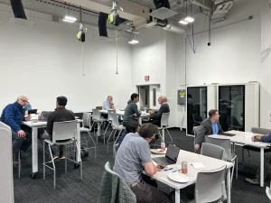 A spacious room with several tables and chairs, where people are engaged in discussions and working on laptops.