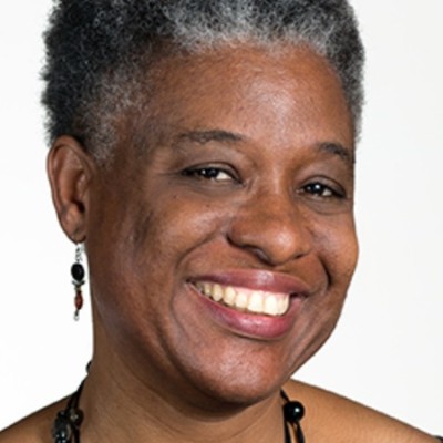 A smiling woman with short gray hair and earrings, wearing a black necklace. She has a warm expression and is facing the camera