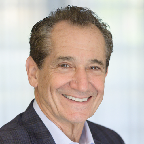A middle-aged man with short, dark hair and a friendly smile is wearing a dark blazer over a light shirt. He is facing the camera against a softly blurred background
