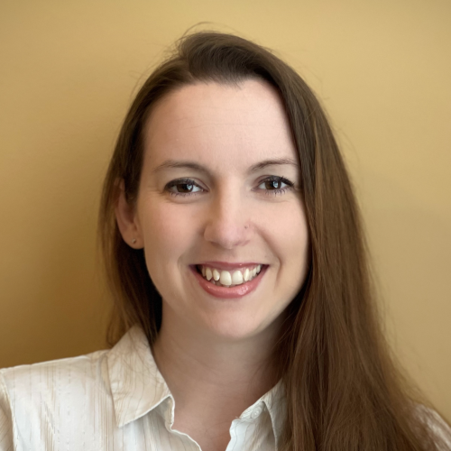 A woman with long brown hair smiles at the camera, wearing a white button-up shirt. The background is a warm, solid yellow color